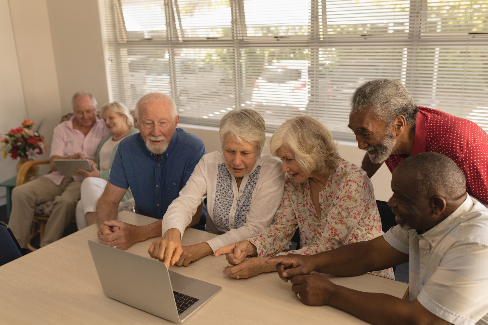 Front view of group of active senior people using laptop and showing the screen at nursing home